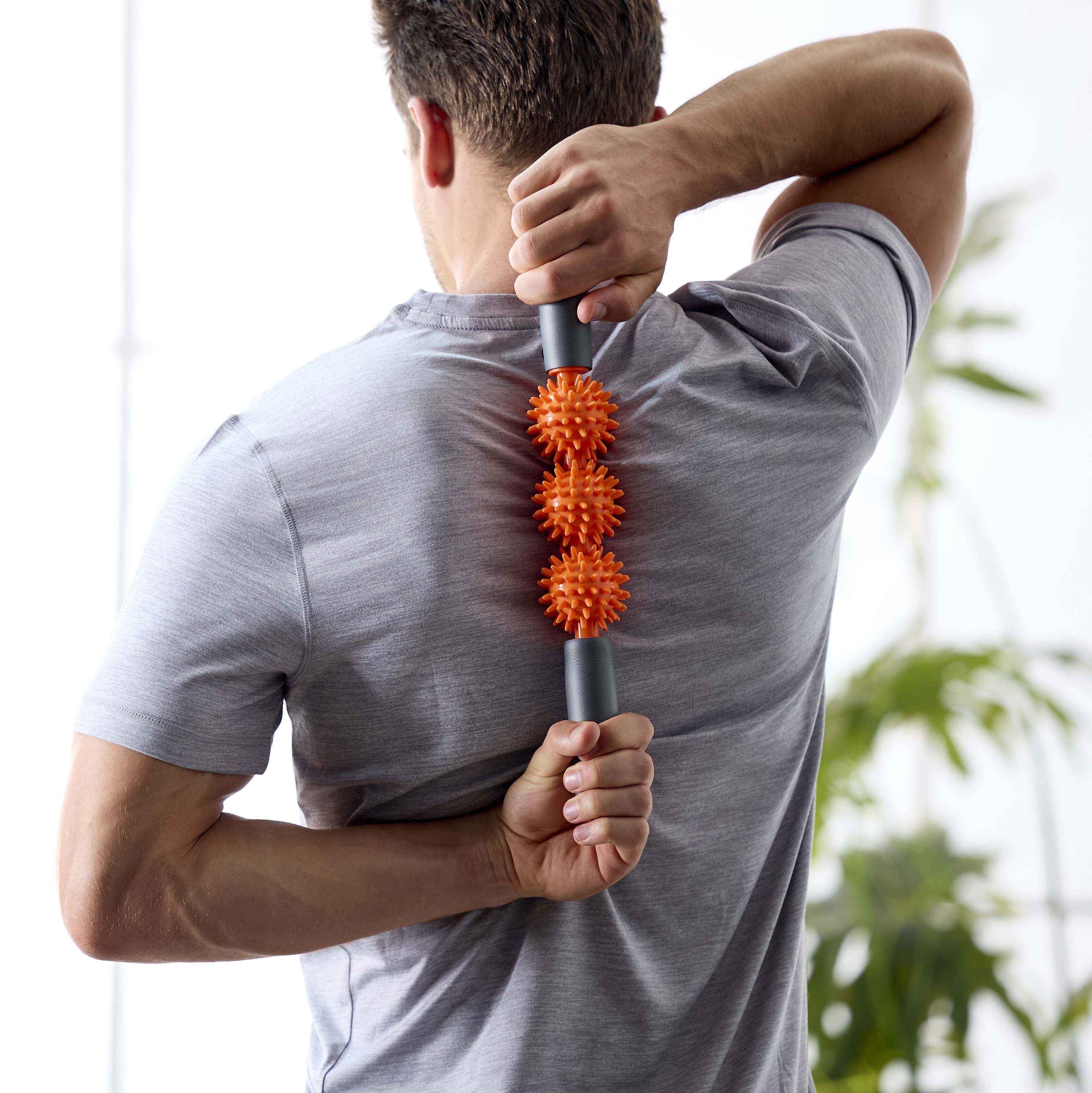 Person standing showing the upper back with the Restore Pressure Point Massager between the shoulder blades being held with both hands